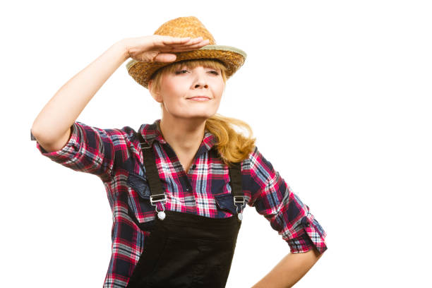 Gardening concept. Attractive woman in dungarees, pink check shirt and sun hat looking into the distance. Isolated background