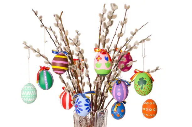 Colored easter eggs on willow bouquet with pussy willows. Religious decoration. Paschal eggs on branches with furry catkins in crystal vase. Salix. Front view, horizontal, on white background. Photo.