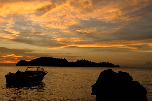 As the sun sets over Krabi in Thailand, warm hues of orange and gold reflect off calm waters. A solitary boat floats gently, creating a serene ambiance amidst the picturesque landscape.