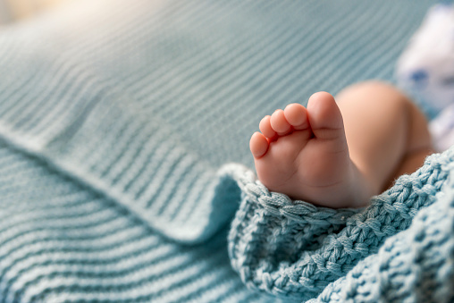 Close up new born infant Caucasian baby feet. Photo of tiny adorable bare pink baby feet as the infant sleeps. Baby toes. Childhood. Motherhood. Legs of unrecognizable newborn baby boy. Portrait of a children's feet in the bedroom during bright sunny day.