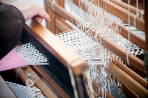 Close-up view of old traditional loom, senior woman's hand working, thread from weaving machine. Galicia, Spain.