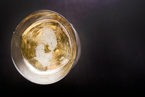 High angle view of white wine in wineglass, champagne with bubbles, close-up view, copy space on the right, black background.