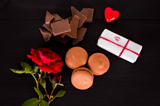 istock Chocolate macaroons, gift and rose flower on a dark background. 914072984