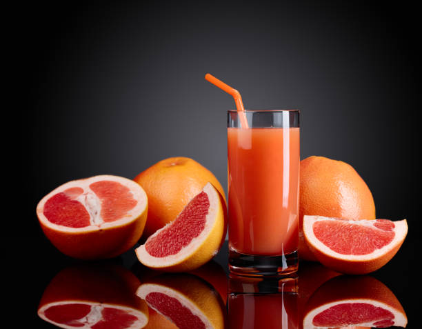 Glass of  grapefruit juice and cut fruits on black background.