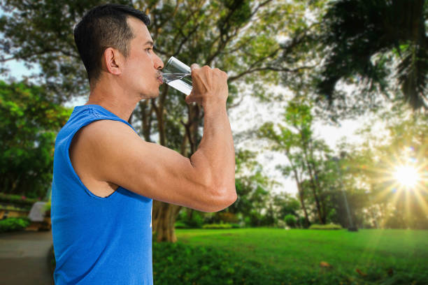 istock Man drinking water from glass after exercise on blurred nature background with soft sunlight, health care concept 914083282