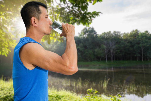 istock Man drinking water from glass after exercise on blurred nature background with soft sunlight, health care concept 914085312