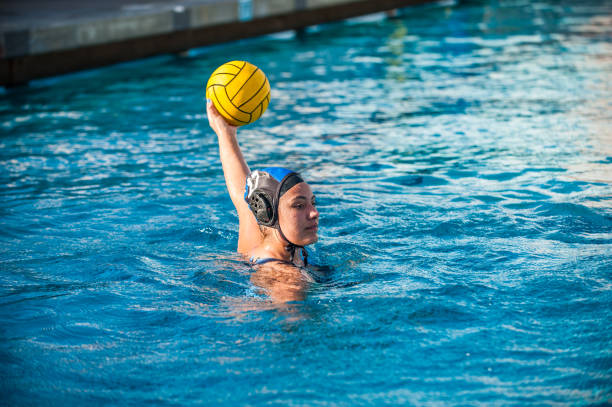 Playing offense in the pool High School female water polo player holding ball high above the water looking to pass or shoot. water polo stock pictures, royalty-free photos & images