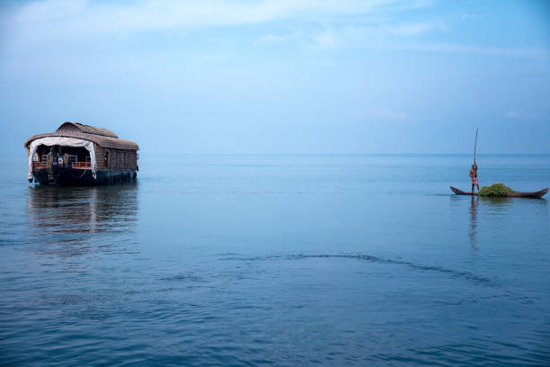 Beautiful trip on one of the floating houseboats in Kerala Backwater. Farmer passing by a houseboat in his small canoe, after having harvested some greens.