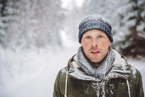 Young handsome bearded man in a warm winter clothes in the winter forest