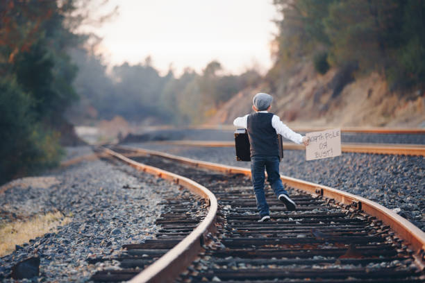 istock Boy Running Down Railroad Tracks With Suitcase and North Pole Sign 914173390
