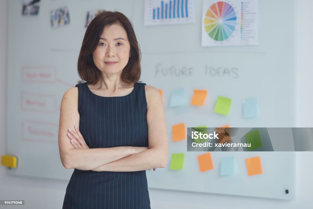 Portrait of businesswoman against whiteboard Portrait of confident businesswoman with arms crossed. Female professional is standing against whiteboard. She is wearing smart casuals. Office Stock Photo