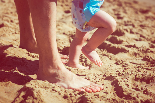 Father teaching baby to walk on summer beach