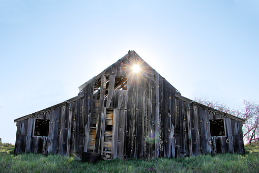 a picture of sun shining through an old weathered barn
