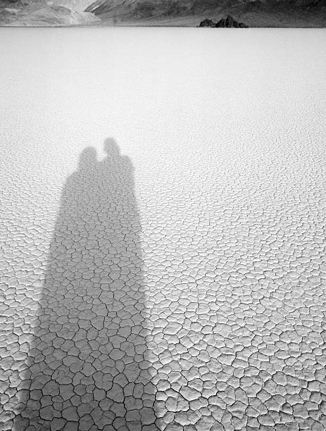 Elongated Shadows of two people strewn across the muddy cracks of the Racetrack in Death Valley, California