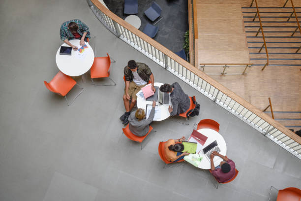 istock Overhead view of students working on laptops in modern college interior 914314280