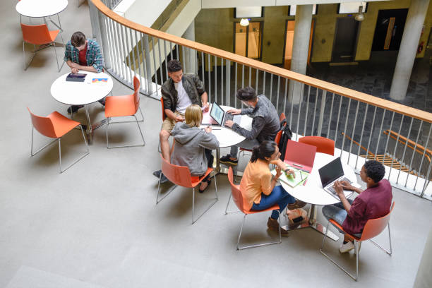 istock Students sitting at tables using laptops and meeting friends 914314292