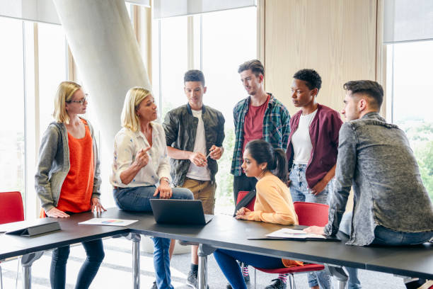 sei studentesse universitarie che ascoltano docente matura con laptop in classe - lettore foto e immagini stock