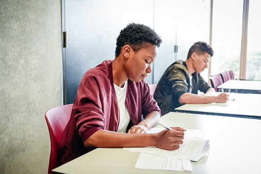 Two young people sitting at desks side by side in classroom doing exam