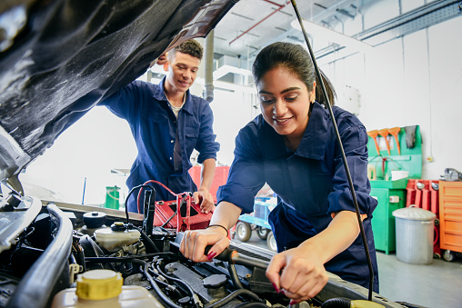Two car mechanic students working in garage at FE college, young woman learning mechanical skills