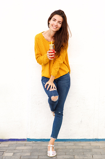 Full portrait of attractive young woman standing outdoors with juice