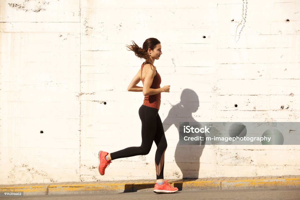 Side portrait of fit young woman running outdoors Full length side portrait of fit young woman running outdoors Jogging Stock Photo