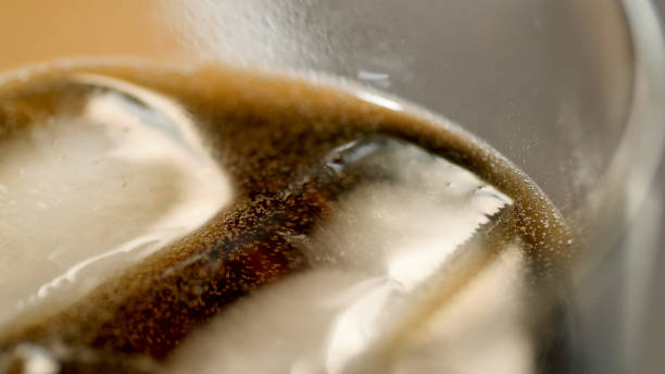 istock Closeup view of glass with dark cocktail drinks and ice cubes in it making bubbles 914327144