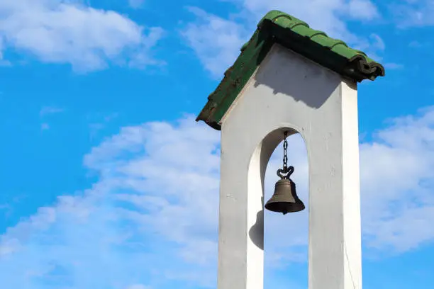Churchbell in white wall of church tower. Catholic church building. Catholic religious architecture detail. White stone tower with bell. Traditional religious building. White cathedral bell tower