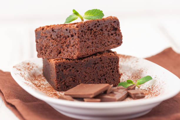 istock Chocolate brownie square pieces in stack on white plate decorated with mint leaves and cocoa powder on white vintage wooden background. American traditional delicious dessert. Close up photography 914330806