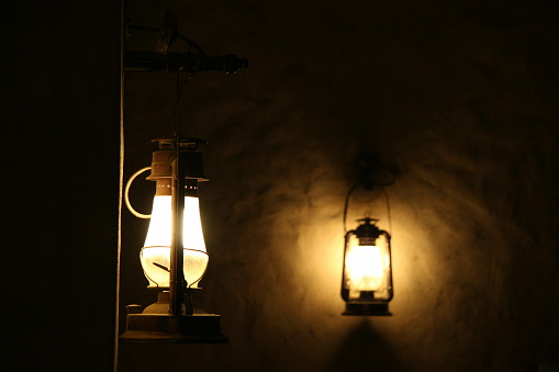 Illuminated lighting of The old vintage table lamp with daisies bouquet in glass vase on round table beside concrete and brick wall in retro restaurant