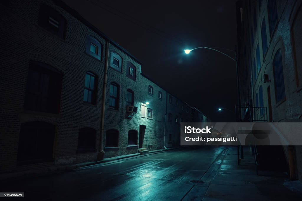 Ruelle de ville urbain sombre dans la nuit après une pluie, mettant en vedette des entrepôts vintage. - Photo de Nuit libre de droits