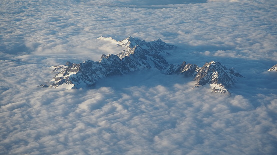 The peaks of the mountains sprout from the clouds that cover the earth. Landscape from the airplane window