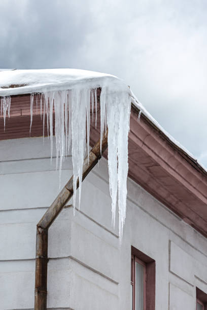 tetto di edificio coperto di neve e ghiaccioli strapiombanti - icicle hanging snow moving down foto e immagini stock