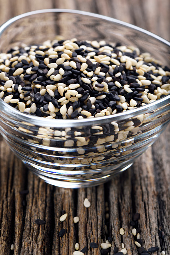 Black and white sesame seeds in a small glass bowl on a wooden background