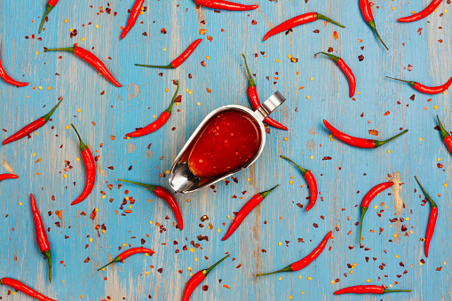 Abstract background with red hot chilli pepper pods, spicy sauce and flakes on blue. Top view