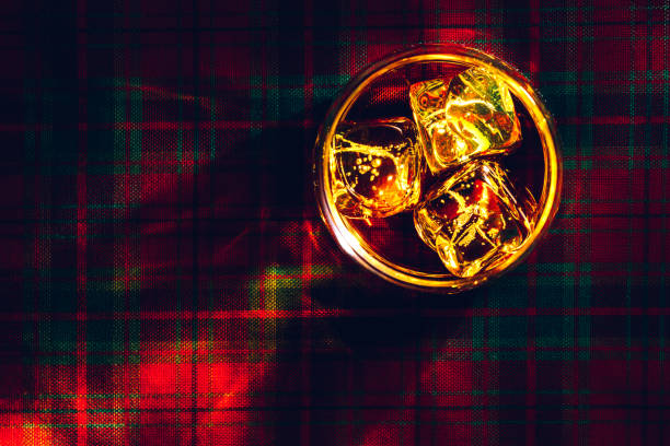 Glass of whisky with ice, on a tartan cloth background.