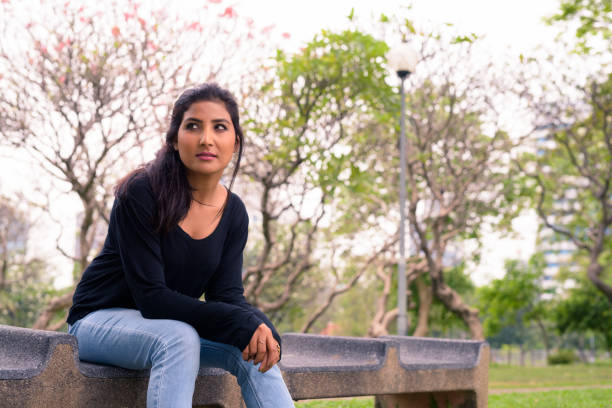 istock Beautiful Indian Woman Sitting At Park Bench 914436144