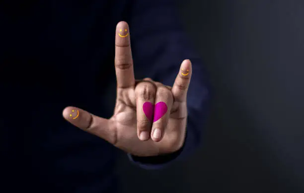 Happiness Love Concept, Midsection Of Man With Colorful Hand Guesture in means "I Love You" with Heart and Smiley Face on Fingers Against Dark Background