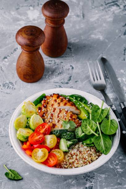 istock Healthy buddha bowl lunch with grilled chicken, quinoa, spinach, avocado, brussels sprouts, tomatoes, cucumbers  on dark grey background. 914439340