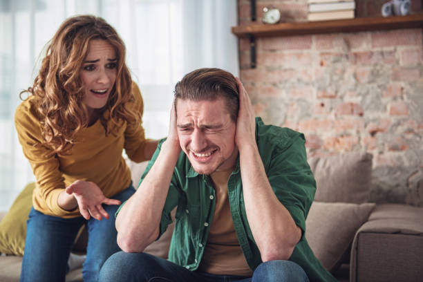 Married couple arguing at home Listen to me. Angry man is closing his ears with desperation while his wife is shouting at him. Family conflict concept man closing ears photos stock pictures, royalty-free photos & images