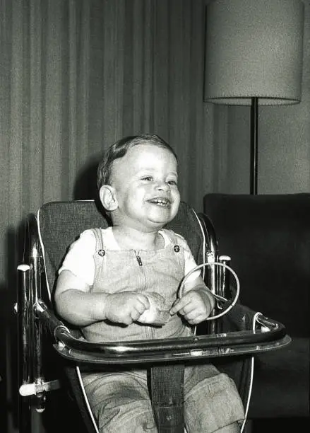 Vintage black and white  image of a cute kid on a baby chair laughing.