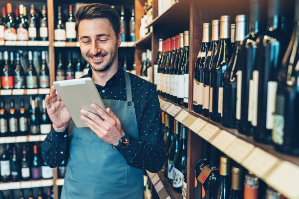 улыбающийся молодой человек с цифровой планшет в винном магазине - wine wine bottle bottle wine rack стоковые фото и изображения