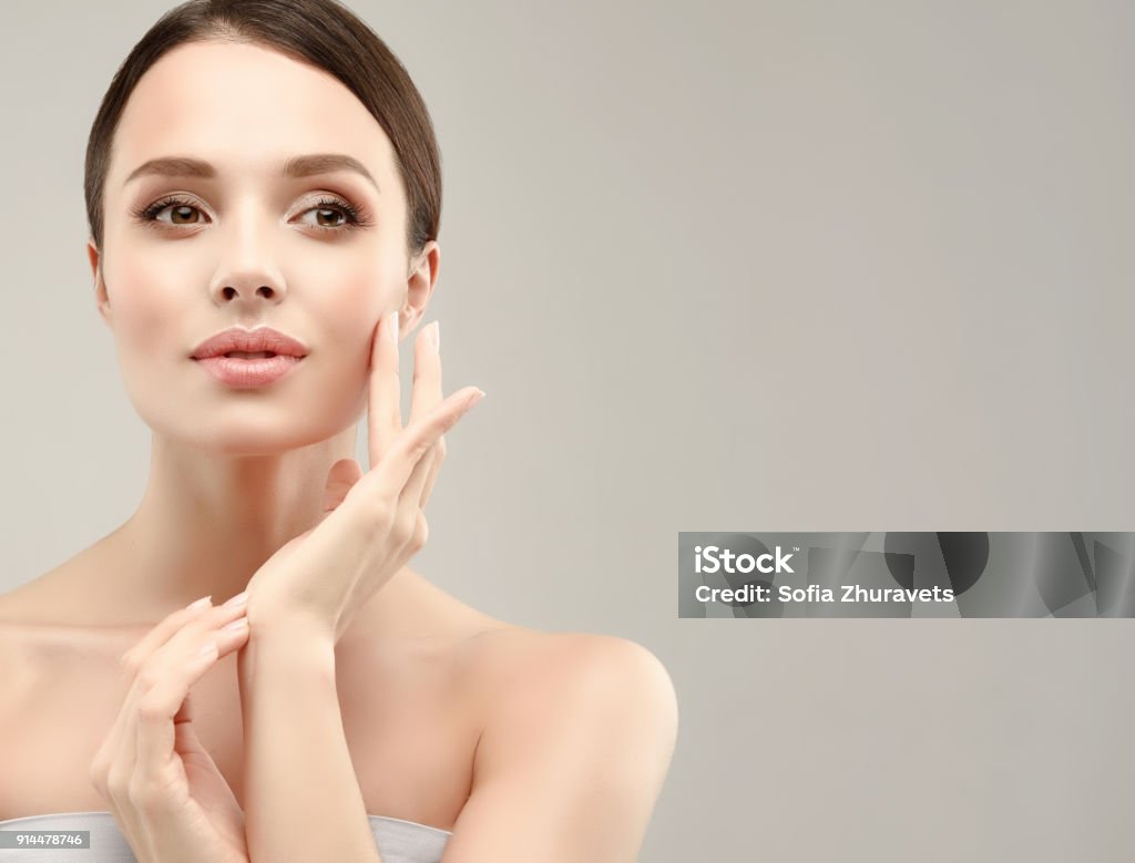 Gorgeous, young woman with clean, fresh skin is touching own face. Cosmetology. Gorgeous, young, blonde haired woman with clean fresh skin is looking straight on camera by magnetic look. Facial treatment, cosmetology, beauty technologies and spa. Human Face Stock Photo