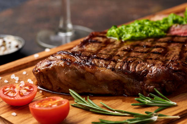 Grilled Black Angus Steak with tomatoes, garlic with chimichurri sauce on meat cutting board. stock photo
