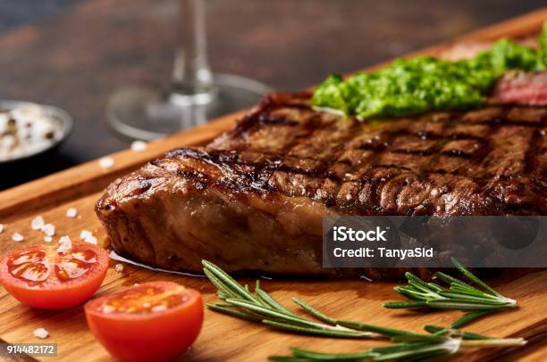 Grilled Black Angus Steak With Tomatoes Garlic With Chimichurri Sauce On Meat Cutting Board Stock Photo - Download Image Now