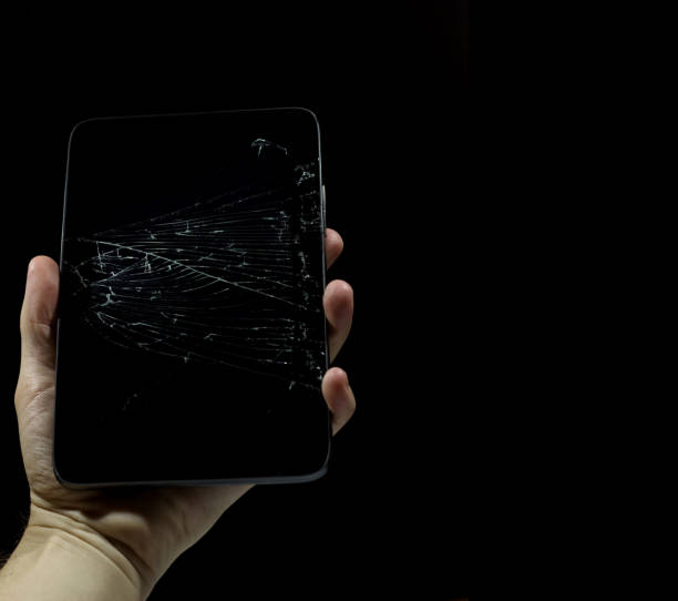 Tablet with a broken screen on a black background. Tablet with a broken screen on a black background. A thin grid of cracks on the glass of the tablet. Copy space. The hand is holding a broken tablet. broken digital tablet note pad cracked stock pictures, royalty-free photos & images