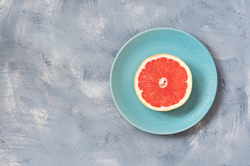 Half of the grapefruit is a blue plate, gray background. Copy space