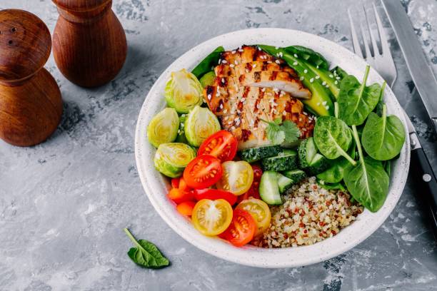 istock Healthy buddha bowl lunch with grilled chicken, quinoa, spinach, avocado, brussels sprouts, tomatoes, cucumbers  on dark grey background. 914524132