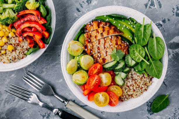 istock Healthy buddha bowl lunch with grilled chicken, quinoa, spinach, avocado, brussels sprouts, tomatoes, cucumbers  on dark grey background. 914524232