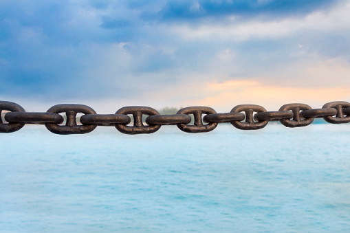 The old rusty chain on sea and sky background. Chain refers to a set of flexible connectors connecting the metal used for seizure or confiscation of objects and draw strength or support.
