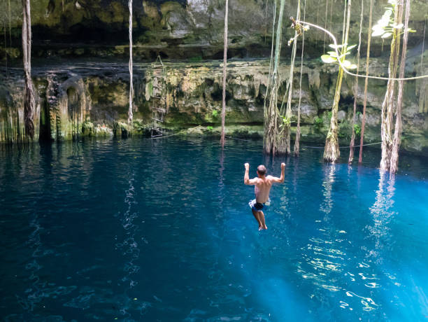 istock Young man rope swinging into Cenote sink hole Oxman 914540832